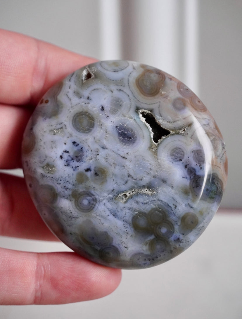 8th vein ocean jasper palm stone with druzy. background is grey with dark grey and brown orbing