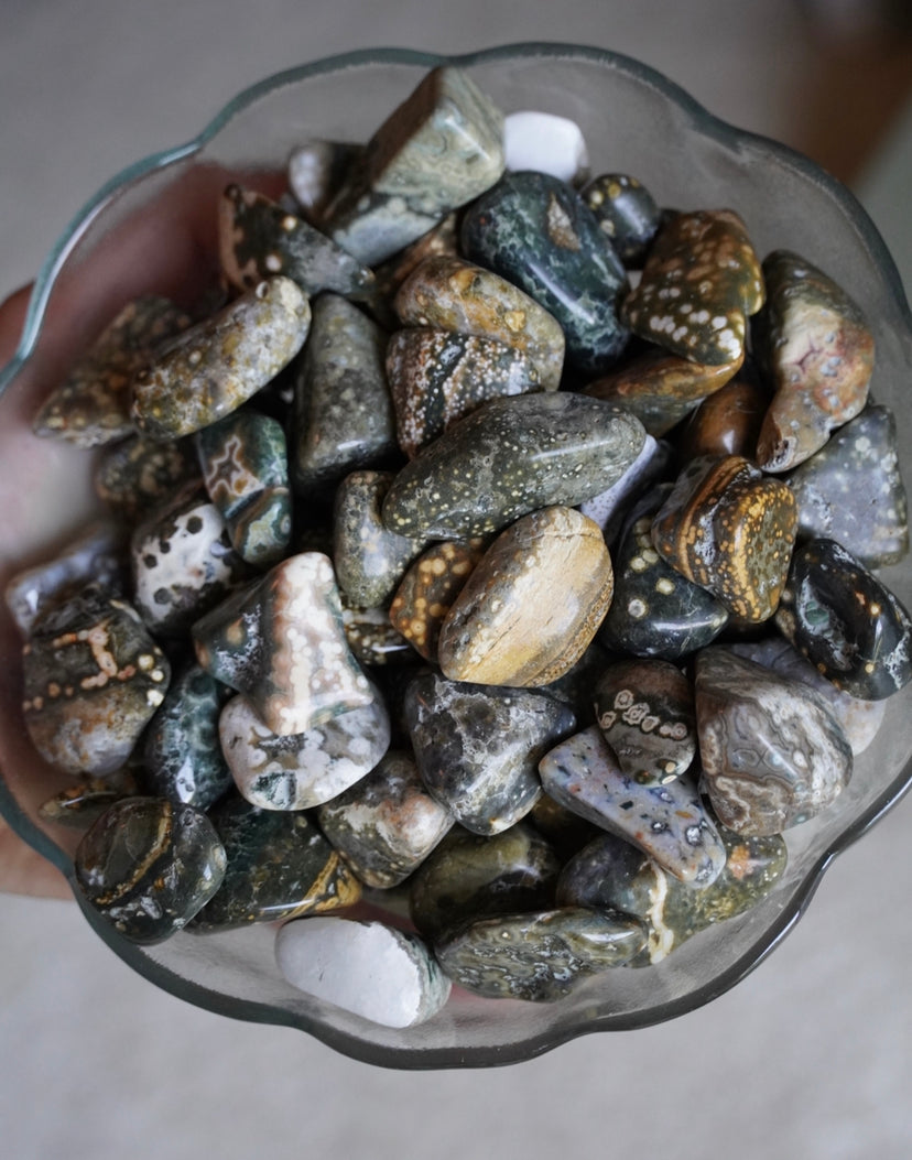 Old stock green, yellow, blue and white colored 7th vein ocean jasper tumbles in a glass bowl 